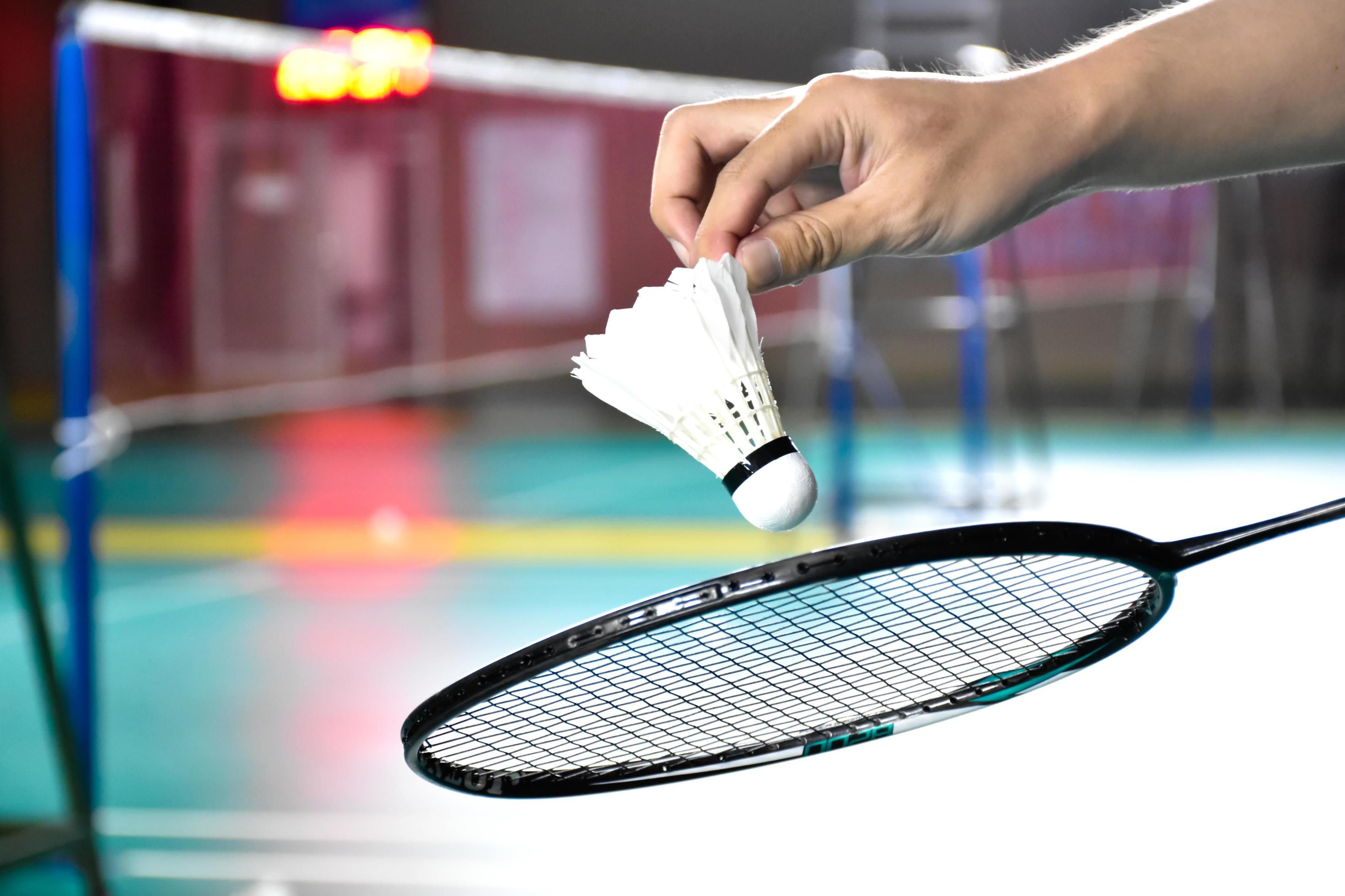 badminton racket and old white shuttlecock holding in hands of player while serving it over the net ahead blur badminton court background and selective focus free photo